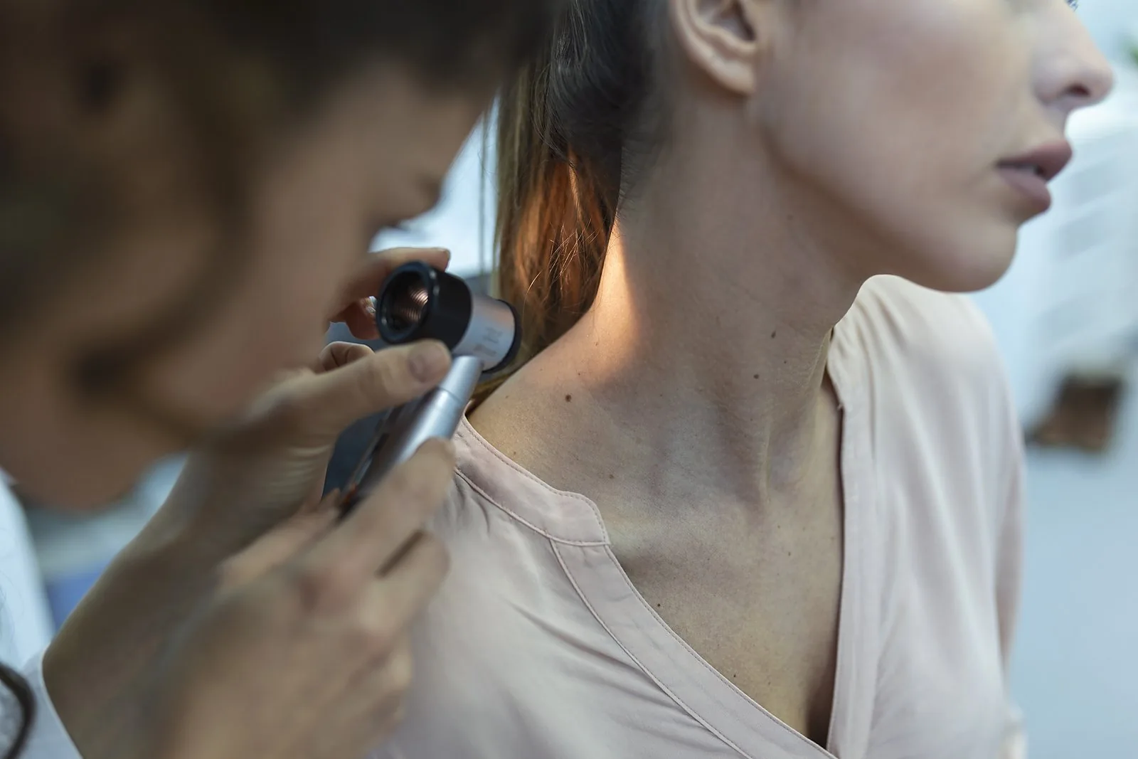 A dermatologist examining moles on a patient's skin with a dermatoscope