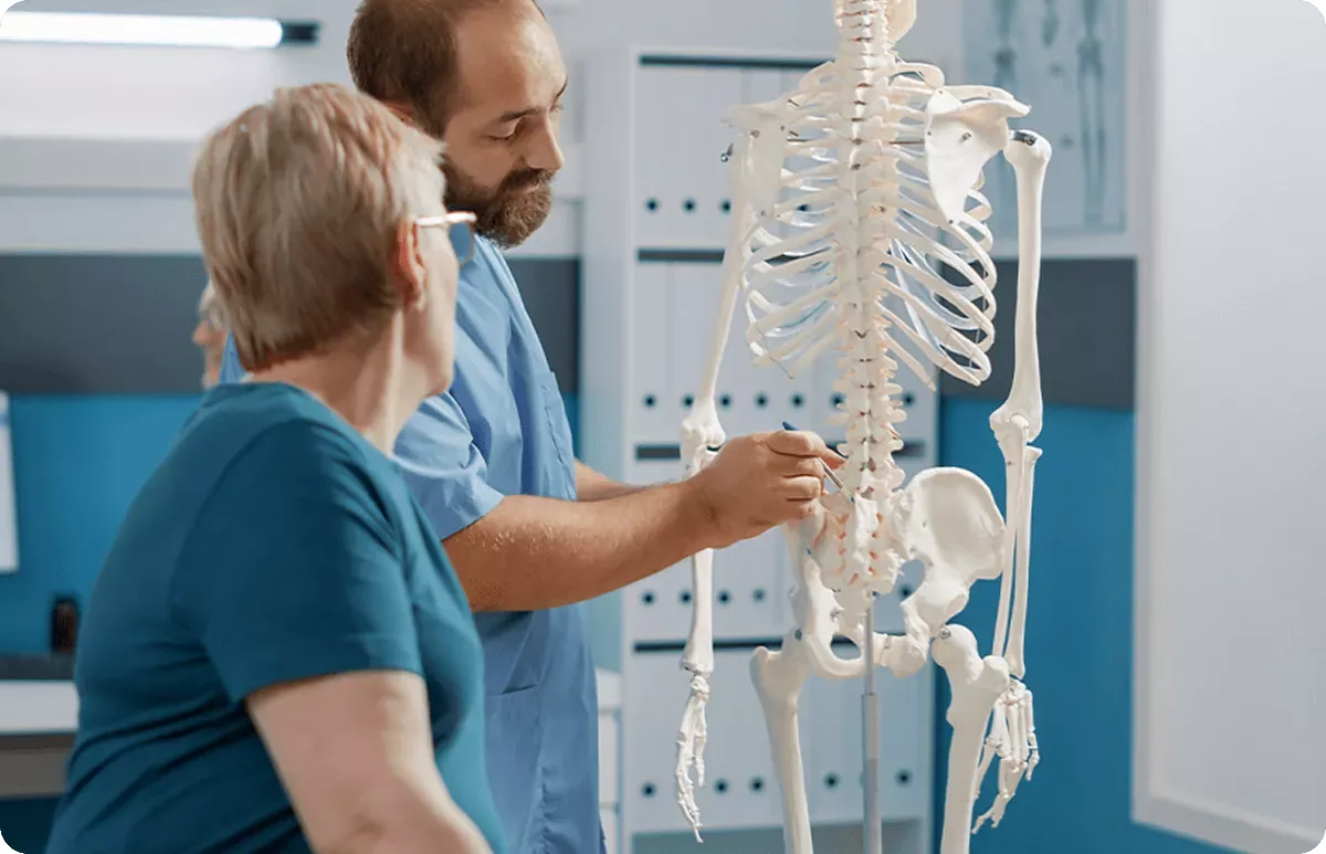 A physiatrist explaining the structure of the spine to a patient using an anatomical skeleton model, a private polyclinic in Belgrade