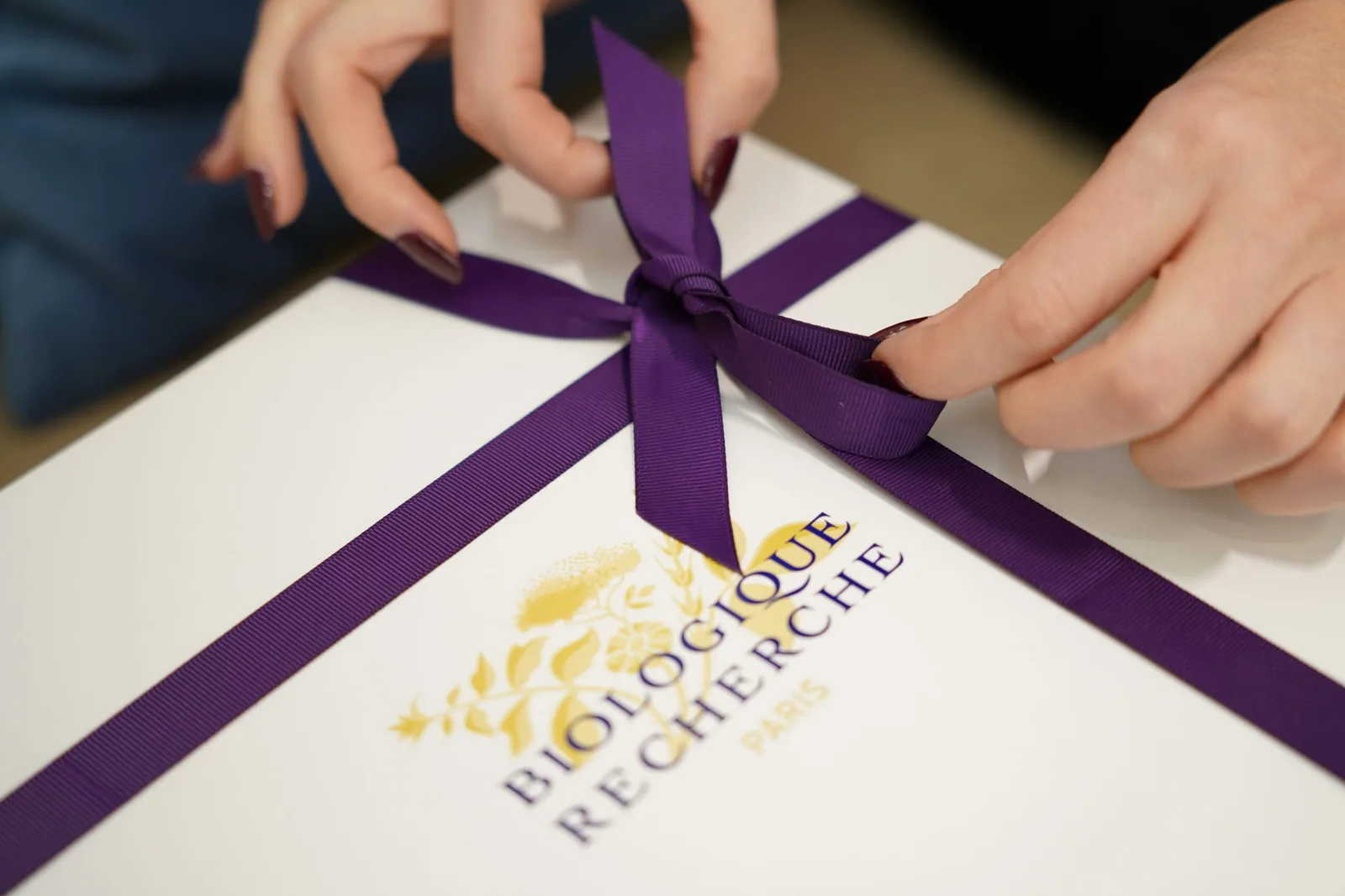 Close up of hands tying a purple ribbon on a Biologique Recherche box at the Miren Medic clinic.