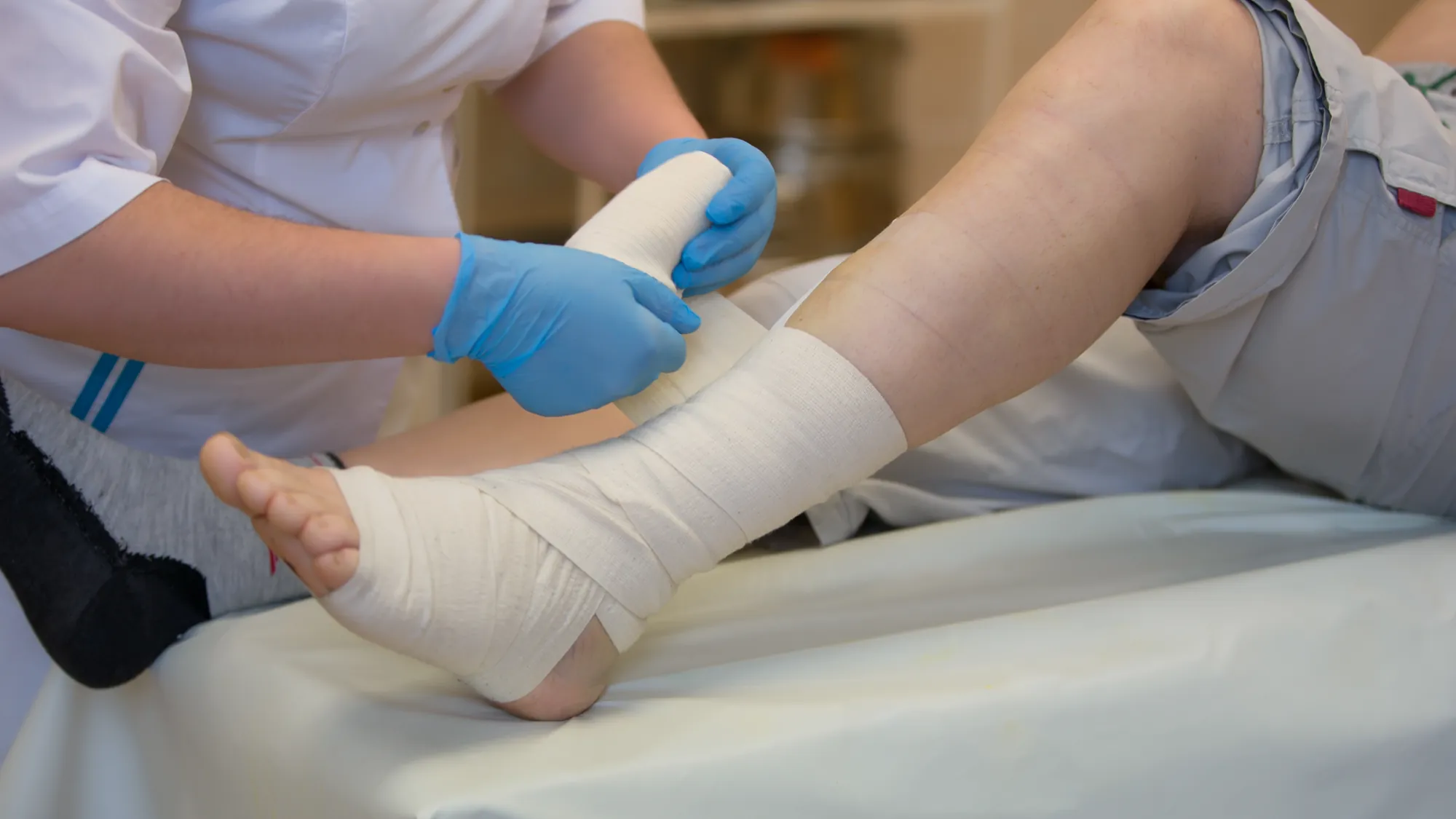 A nurse in gloves dressing a wound on a patient's leg
