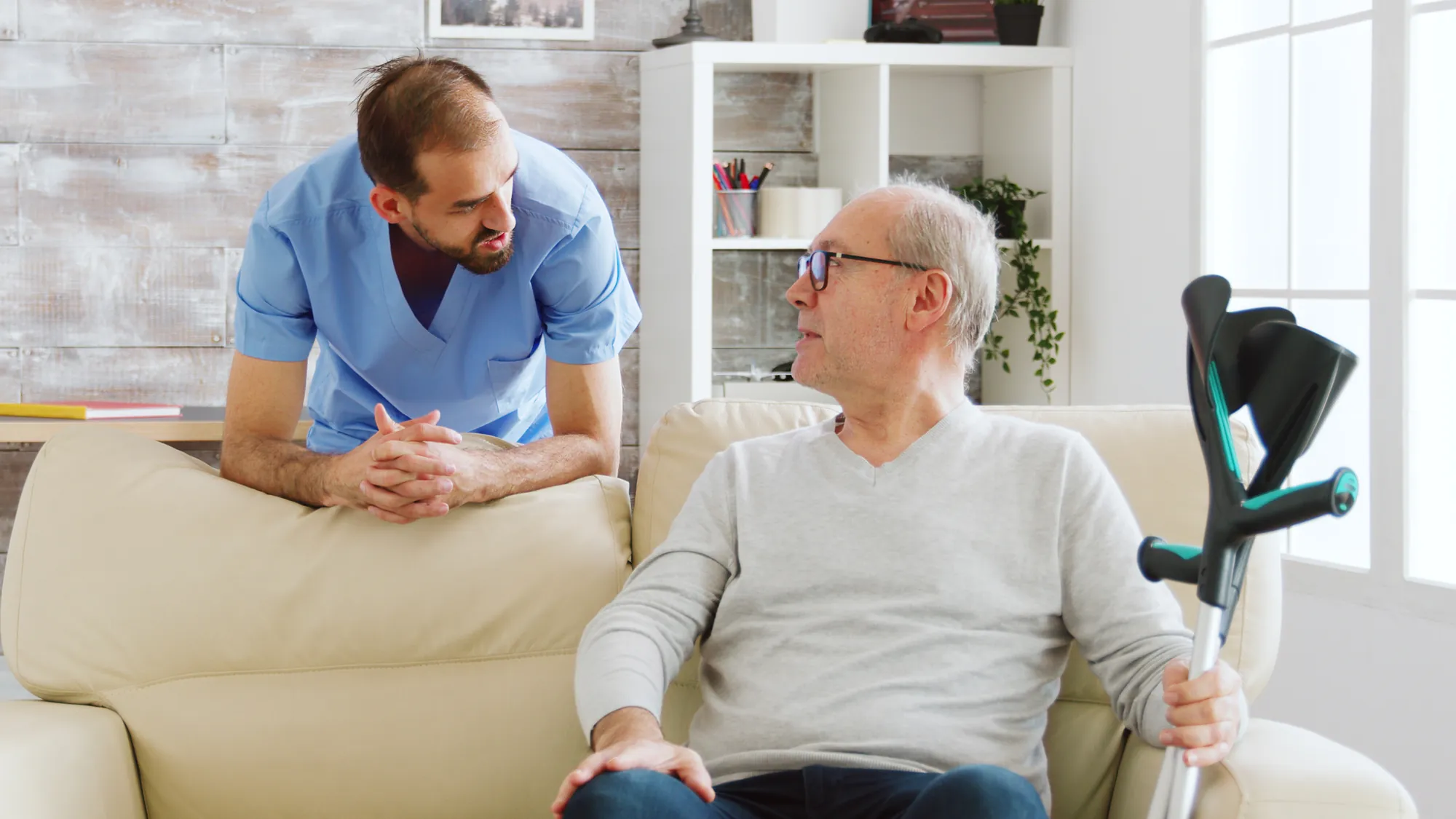 A medical technician on a home visit talking with an elderly patient in the living room