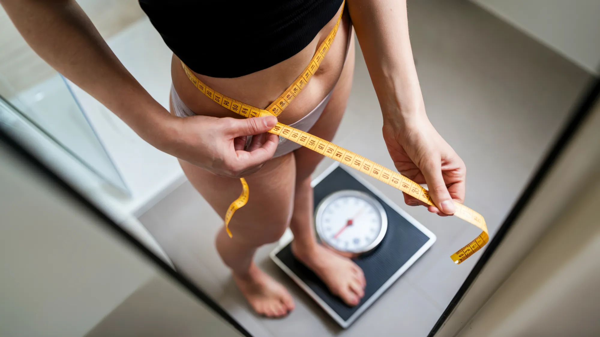 Woman on a scale measuring her waist with a tape measure