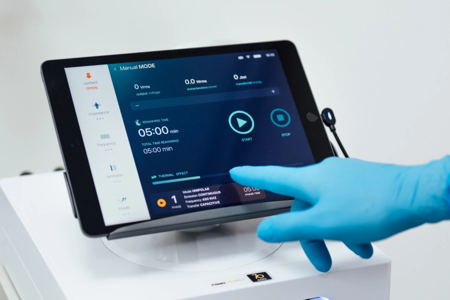 Medicinsko osoblje u plavim rukavicama podešava parametre na digitalnom ekranu savremenog terapijskog uređaja, privatna poliklinika Beograd